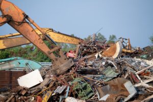Excavator magnet lifting steel scraps from recycling materials pile at scrap yard in recycling