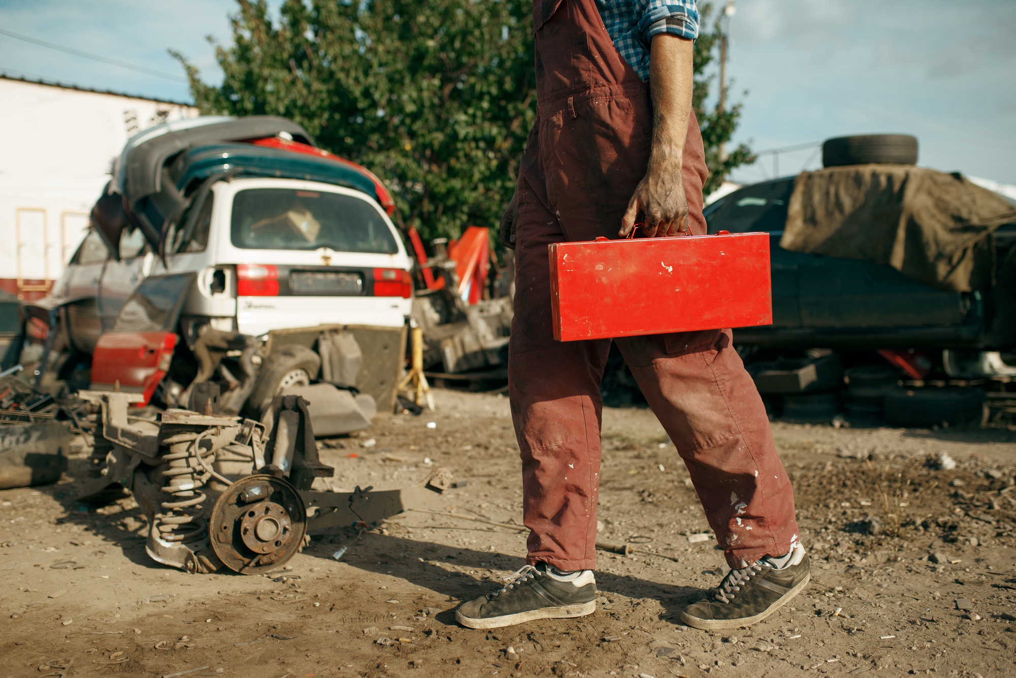 Male repairman holds toolbox on car scrapyard